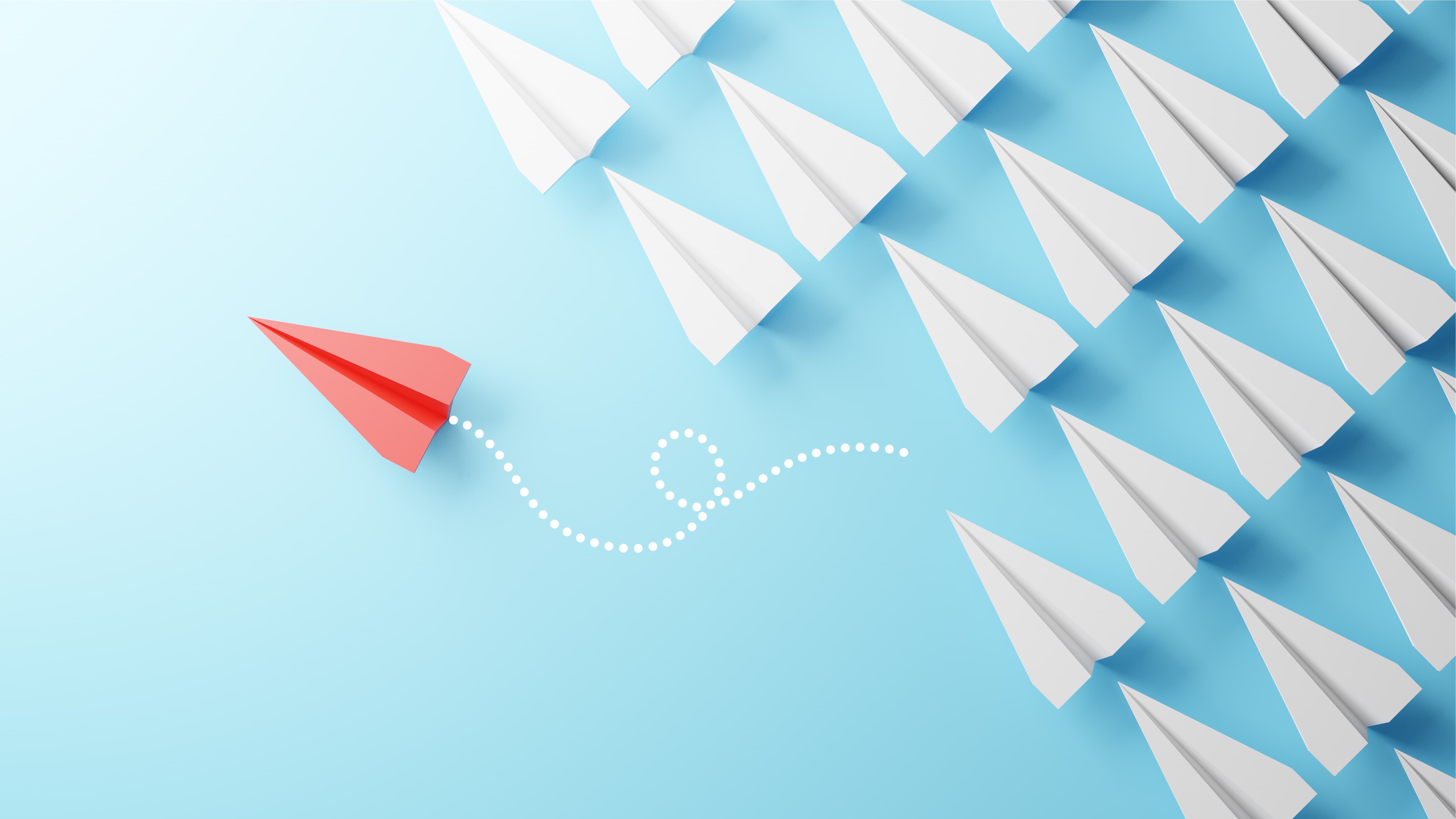 Red paper airplane veering off a dotted path away from a uniform group of white paper airplanes, symbolizing differentiation and standing out from the crowd.